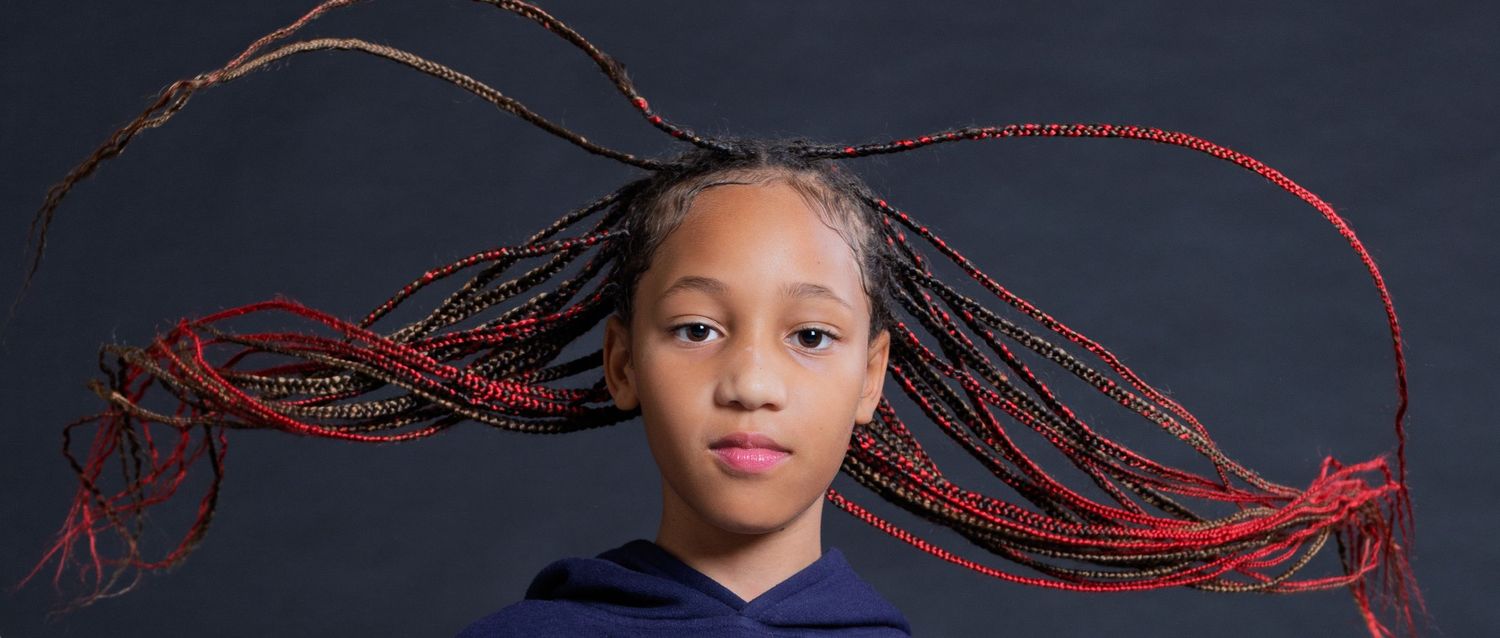 A person wearing a navy blue top with long red braids flowing horizontally against a dark background.