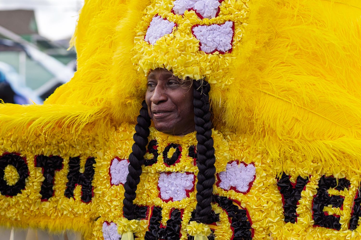 Woman in vibrant yellow feathered Mardi Gras Indian costume with floral decorations at New Orleans festival.