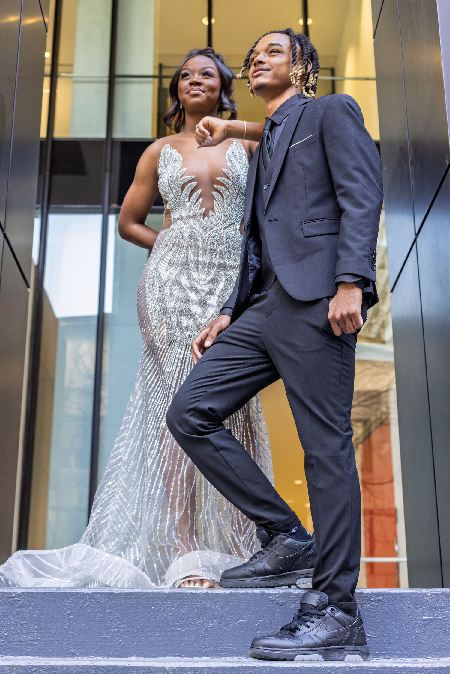 A couple poses on steps, with one wearing a sparkly white mermaid gown and the other in a navy suit.