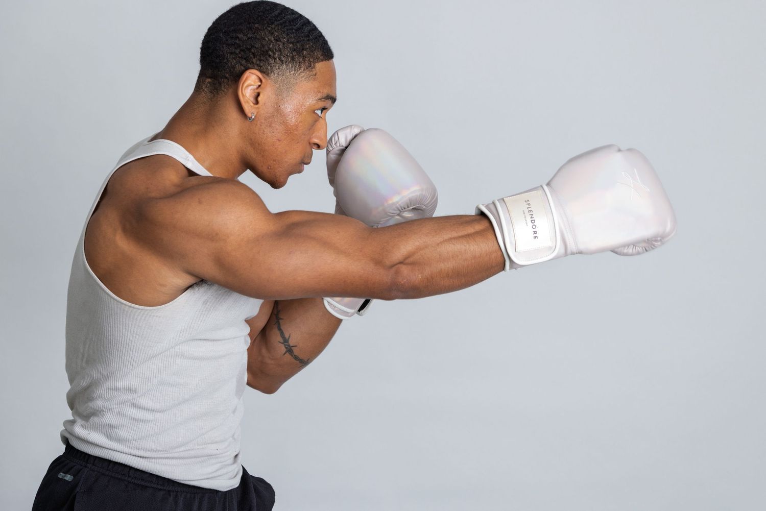 Young athletic man wearing white boxing gloves throwing a punch in a fighting stance against gray background.