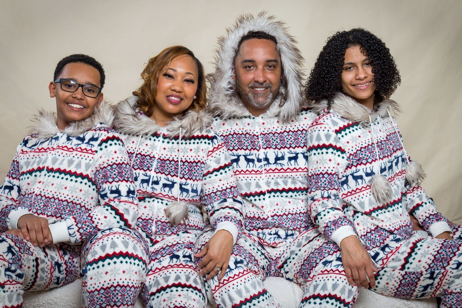 A family wearing matching Christmas pajamas with Nordic patterns poses together on a white couch.