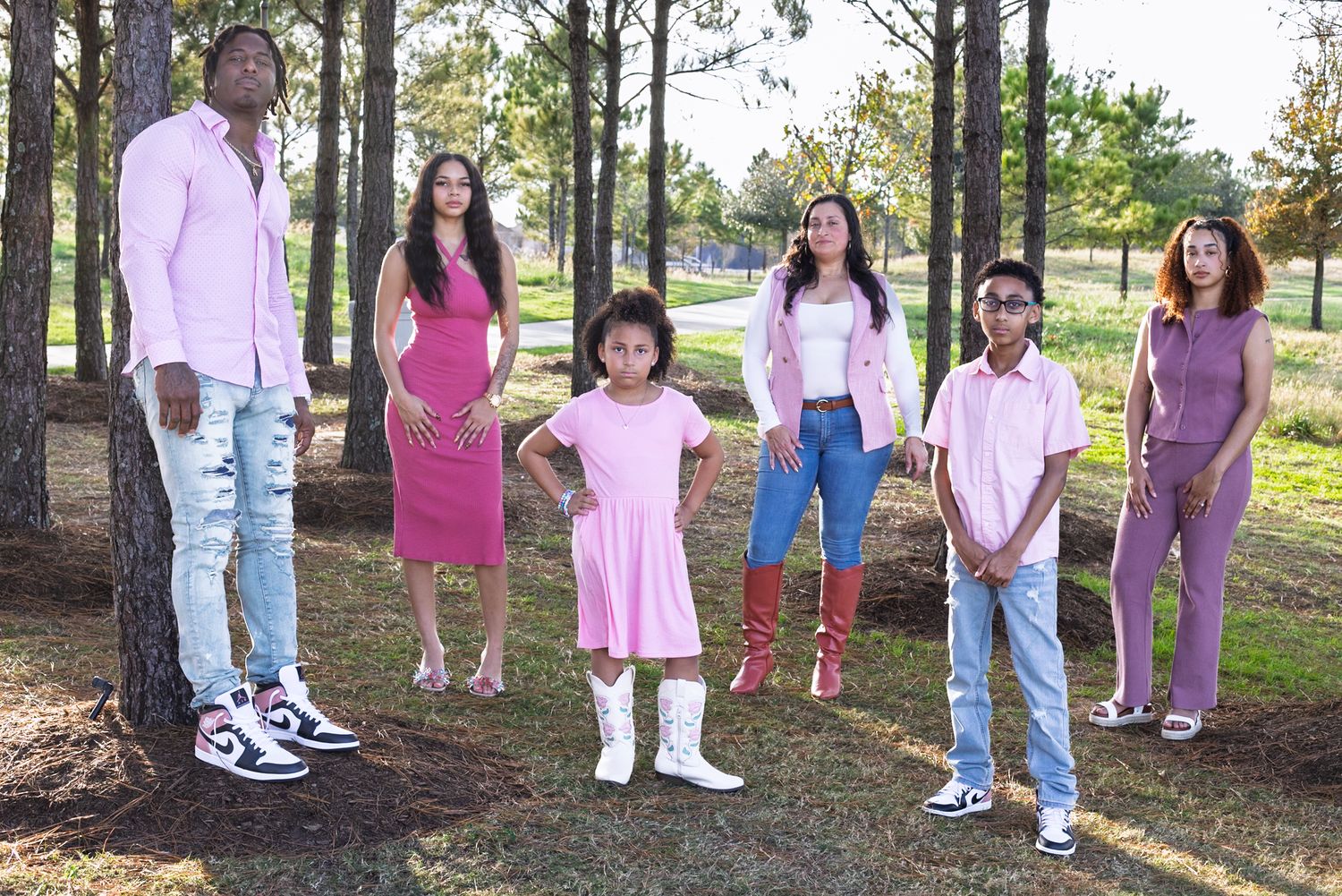 Family of six posing outdoors in coordinated pink outfits among pine trees in a park setting.