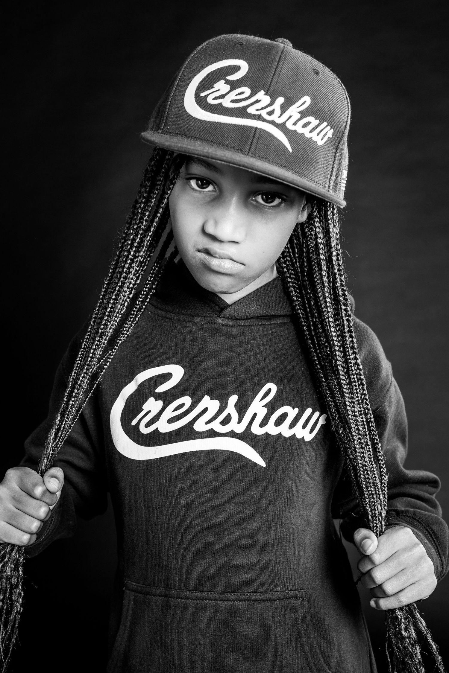 Black and white artistic portrait series showing someone wearing a dark hoodie with cursive lettering and braided hair.