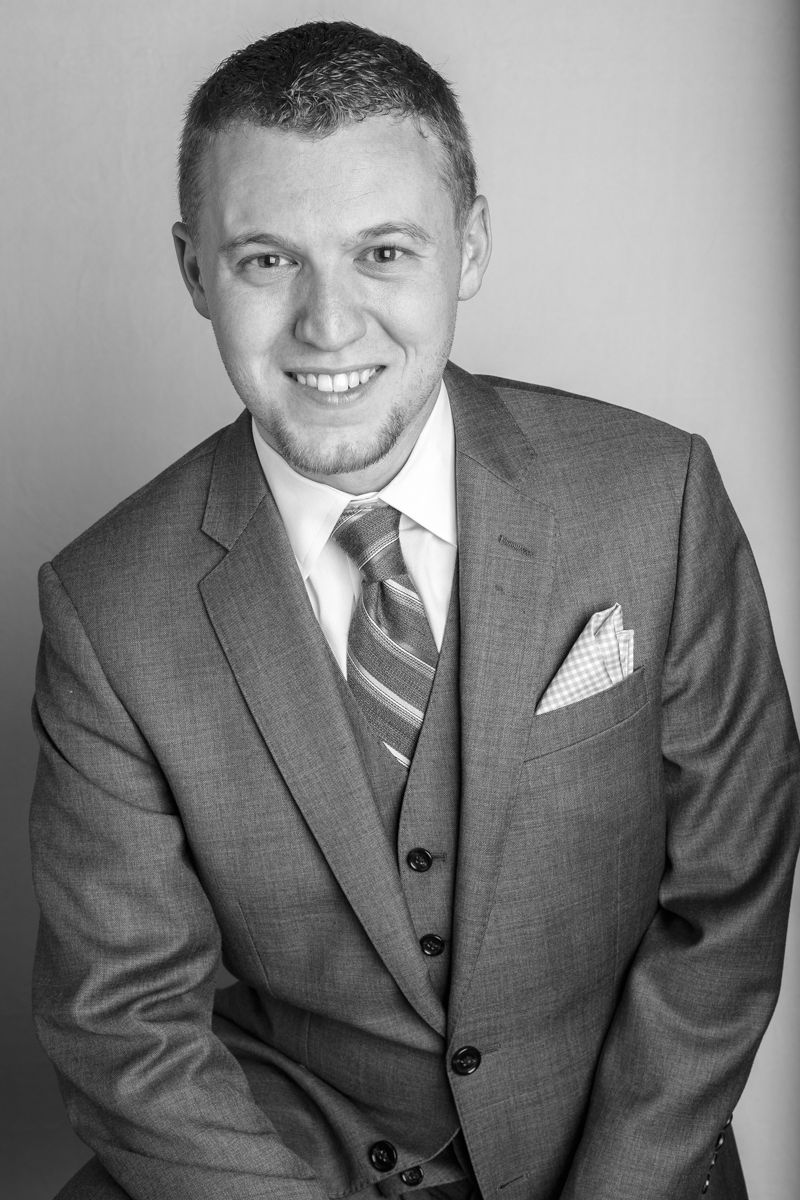 Professional black and white portrait of someone in a three-piece gray suit with striped tie and pocket square.