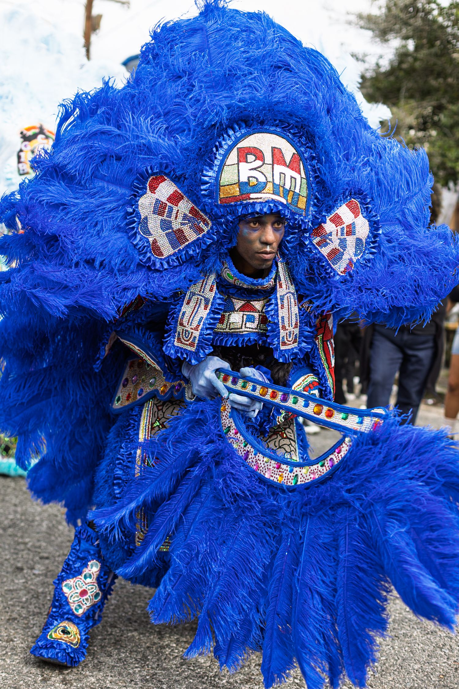 Man in elaborate blue feathered Mardi Gras Indian costume at New Orleans carnival parade.