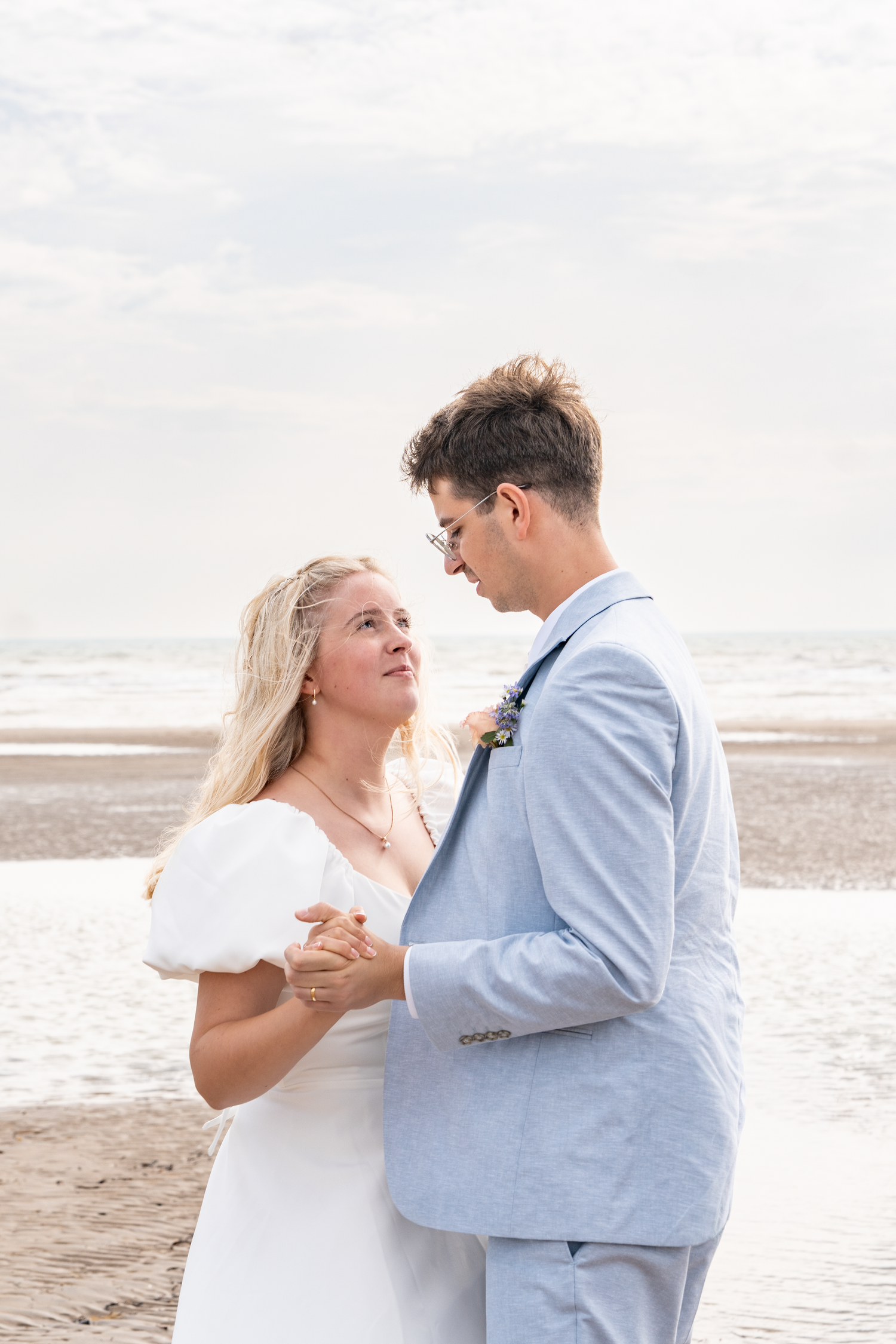 A bride and groom share a romantic dance on a beach, with the ocean and cloudy sky in the background.