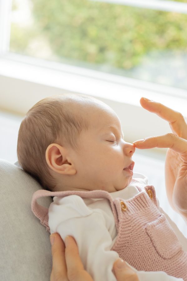 Newborn baby sleeping peacefully in pink knit outfit while parent gently touches nose.