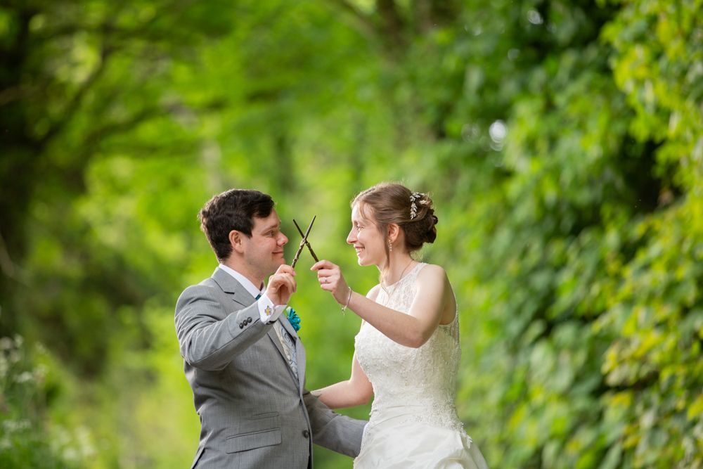 Smiling bride and groom playfully pose together surrounded by lush green foliage on their wedding day.