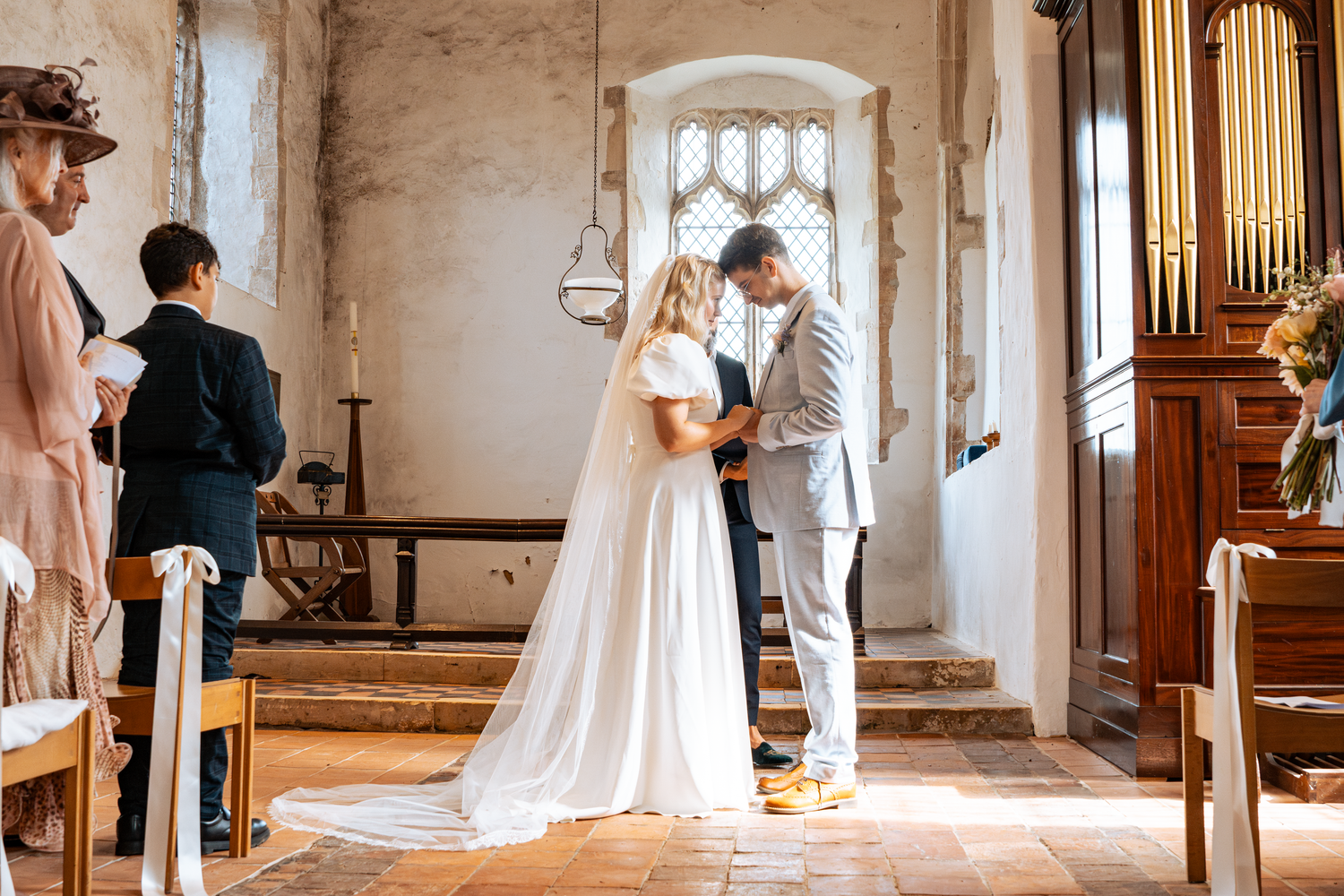 Bride and groom exchange vows at church altar with guests watching in rustic stone chapel with wooden pews.