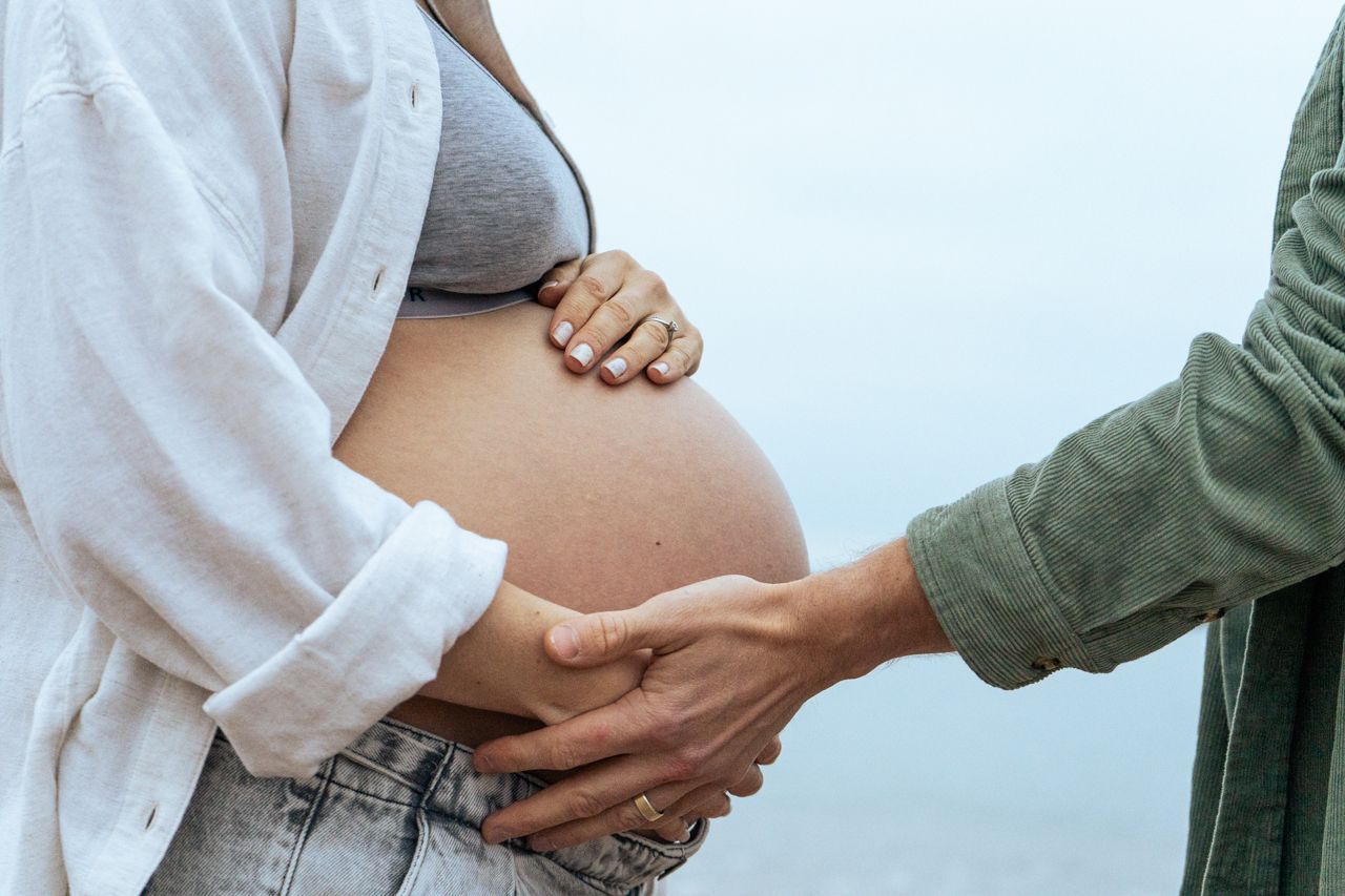 Partner tenderly holding a pregnant woman's bare baby bump outdoors with a soft blurred background.