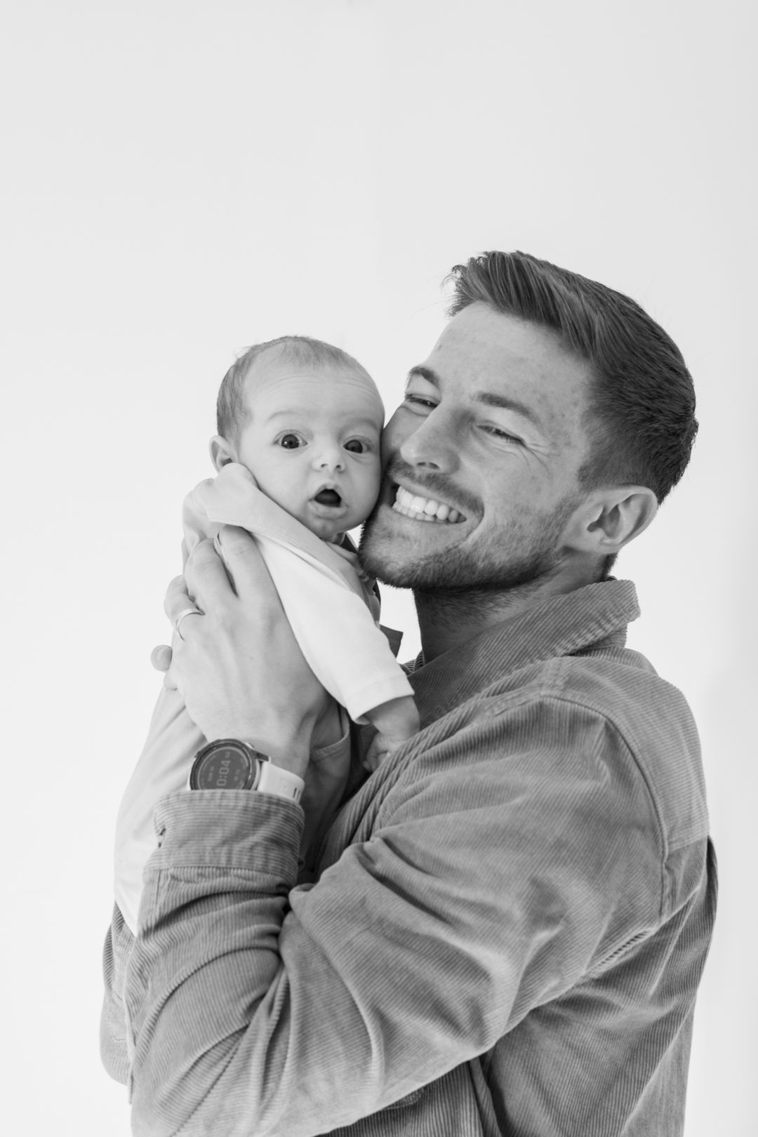 Black and white photo of laughing father holding surprised newborn baby close.