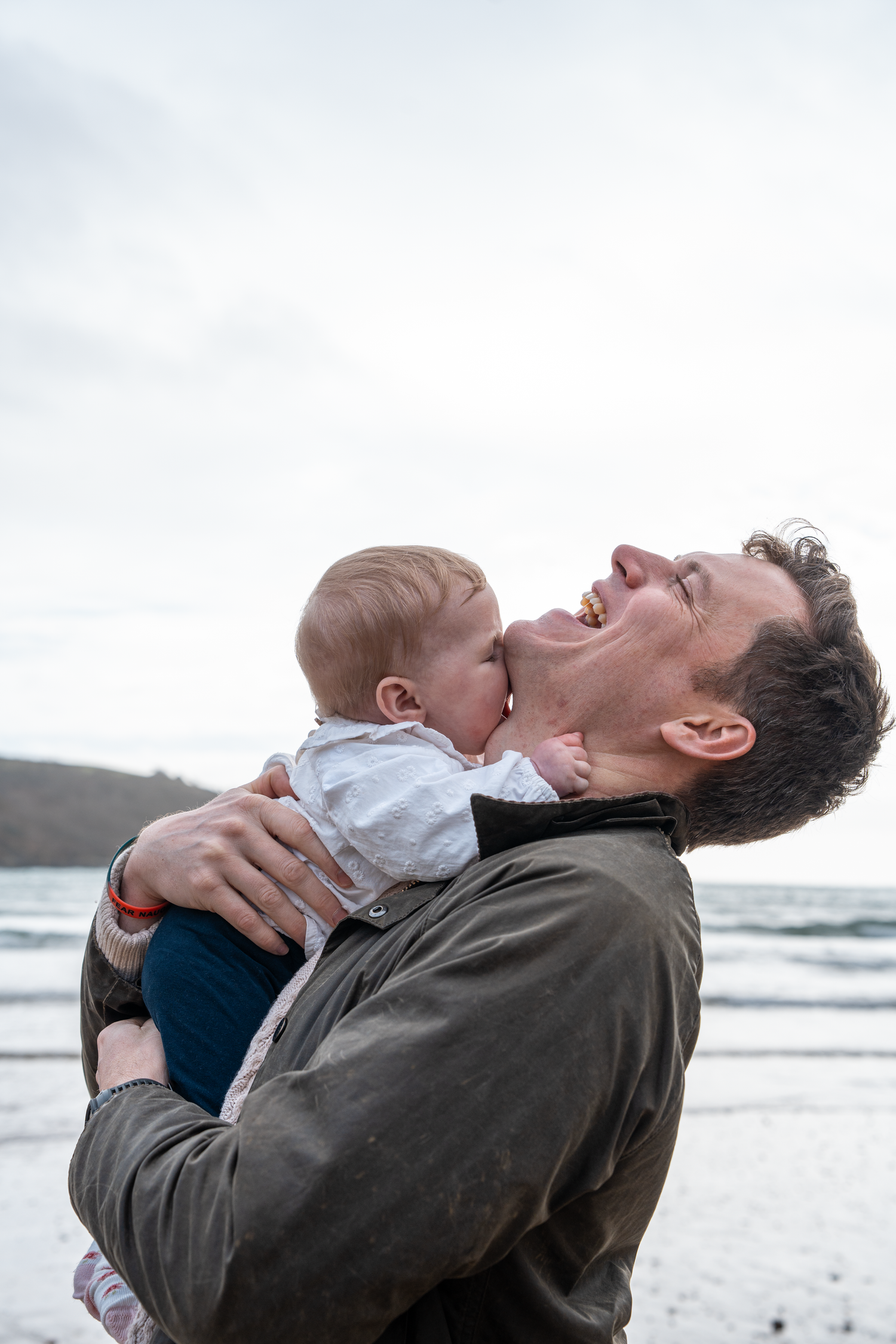 Father laughing joyfully while holding baby at the beach.