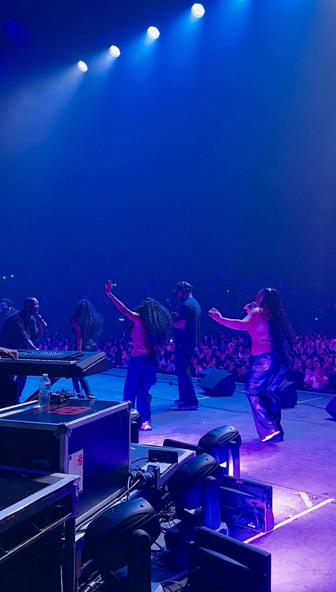 Performers on a concert stage with blue lighting entertaining a large crowd of fans.