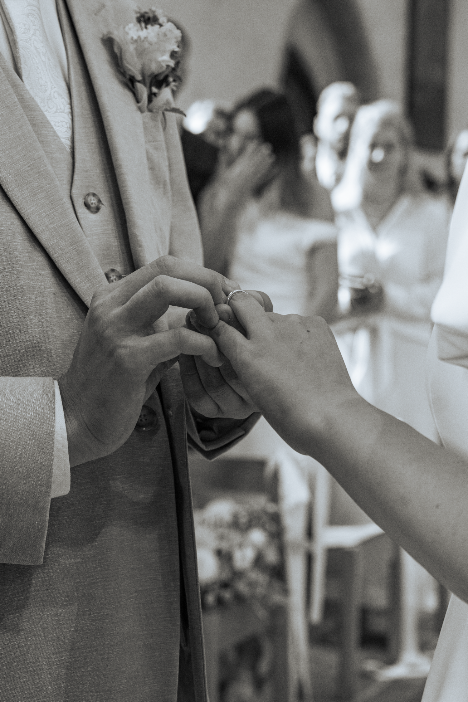 Black and white close-up of bride placing wedding ring on grooms finger during church ceremony.