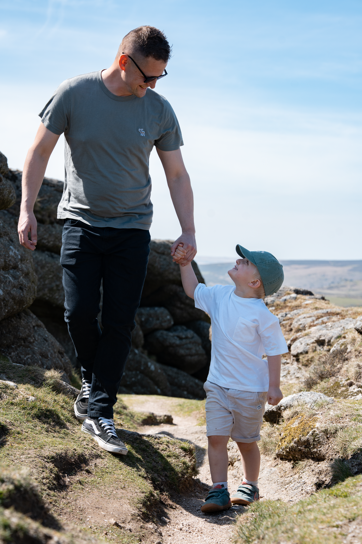 A father and young son holding hands while hiking on a rocky trail on a sunny day.