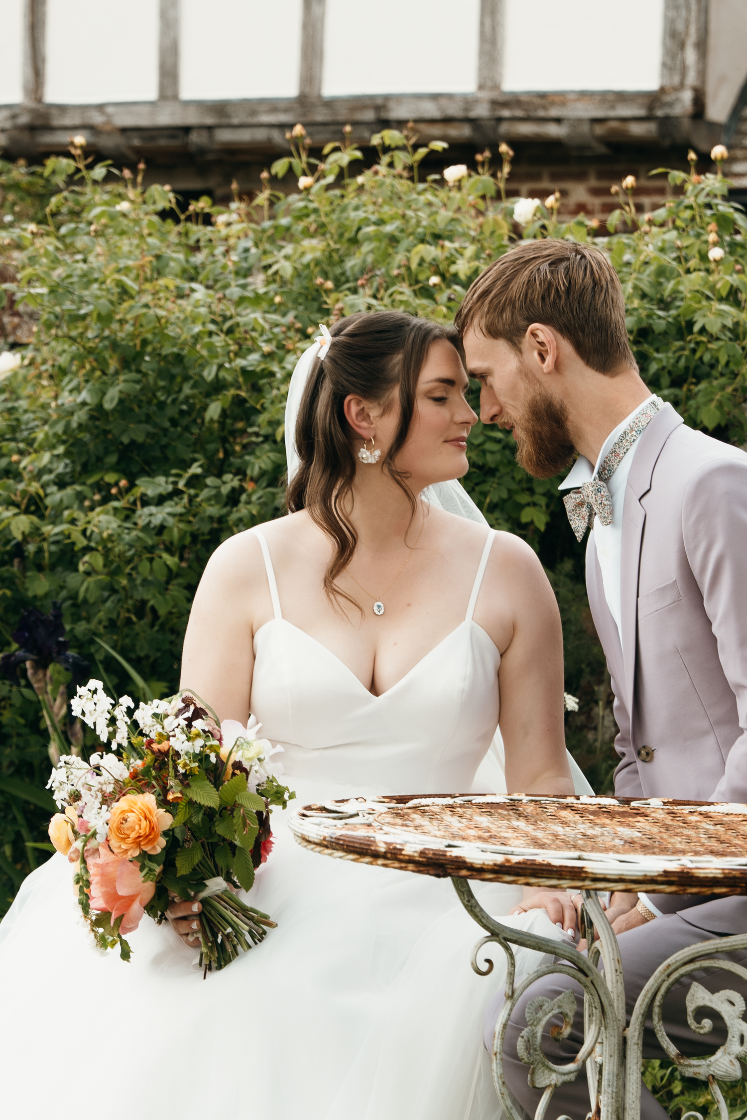 Bride and groom share a romantic moment outdoors, bride holding a colorful bouquet in a white gown.