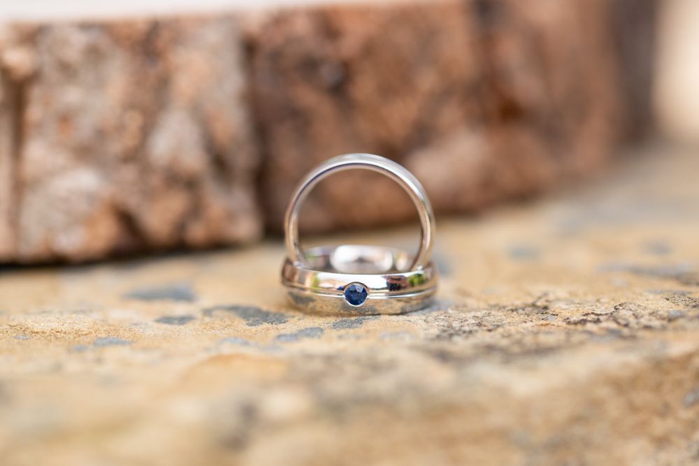 Two silver wedding bands with blue sapphire stones displayed on a rustic stone surface.