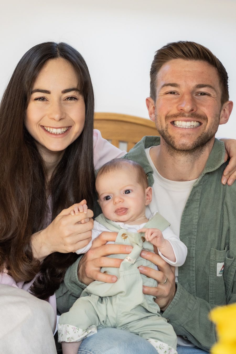 Smiling parents holding their infant baby in green outfit for a family portrait.