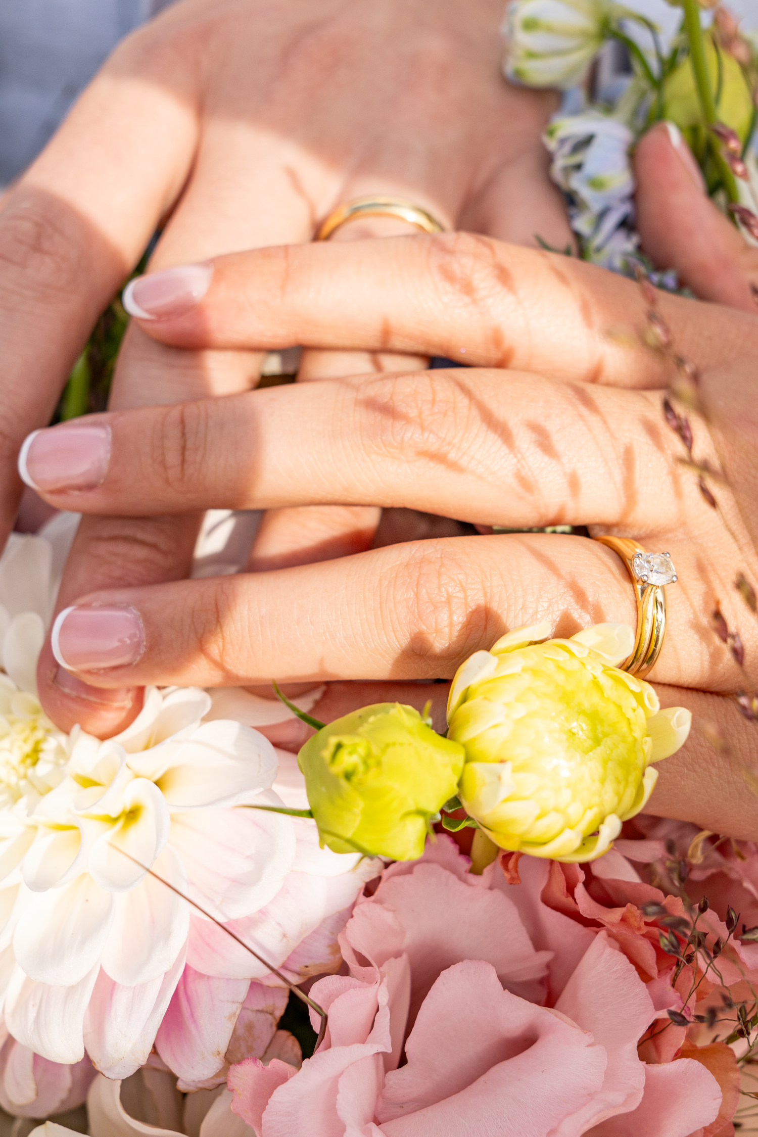 Newlywed couple holding hands showing gold wedding and engagement rings over bridal bouquet.
