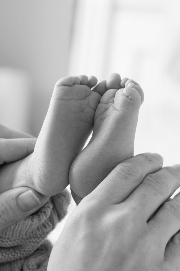 Black and white close-up of a parent's hands gently holding a newborn baby's tiny feet.