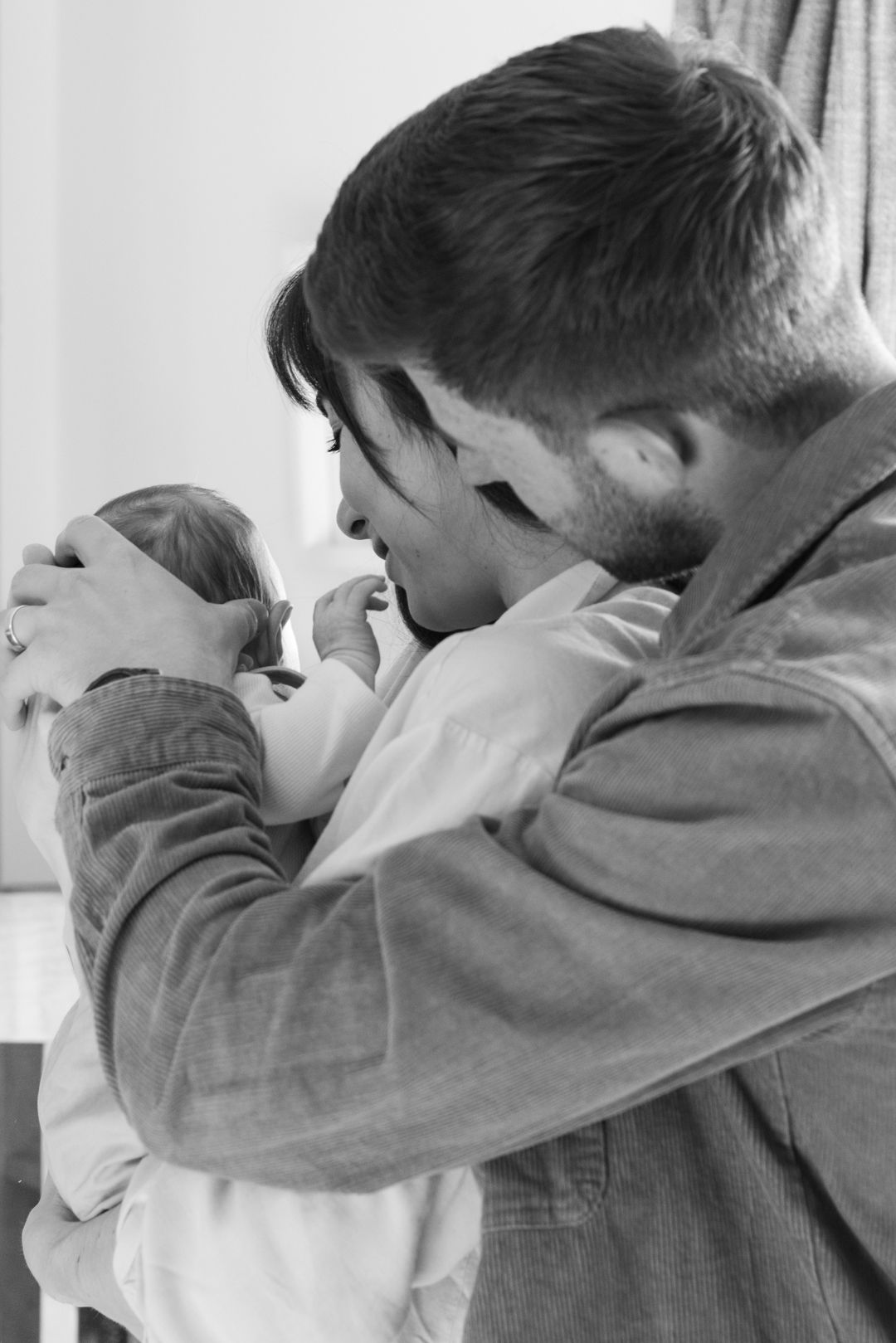 Black and white tender moment of father gently kissing newborn baby's head.