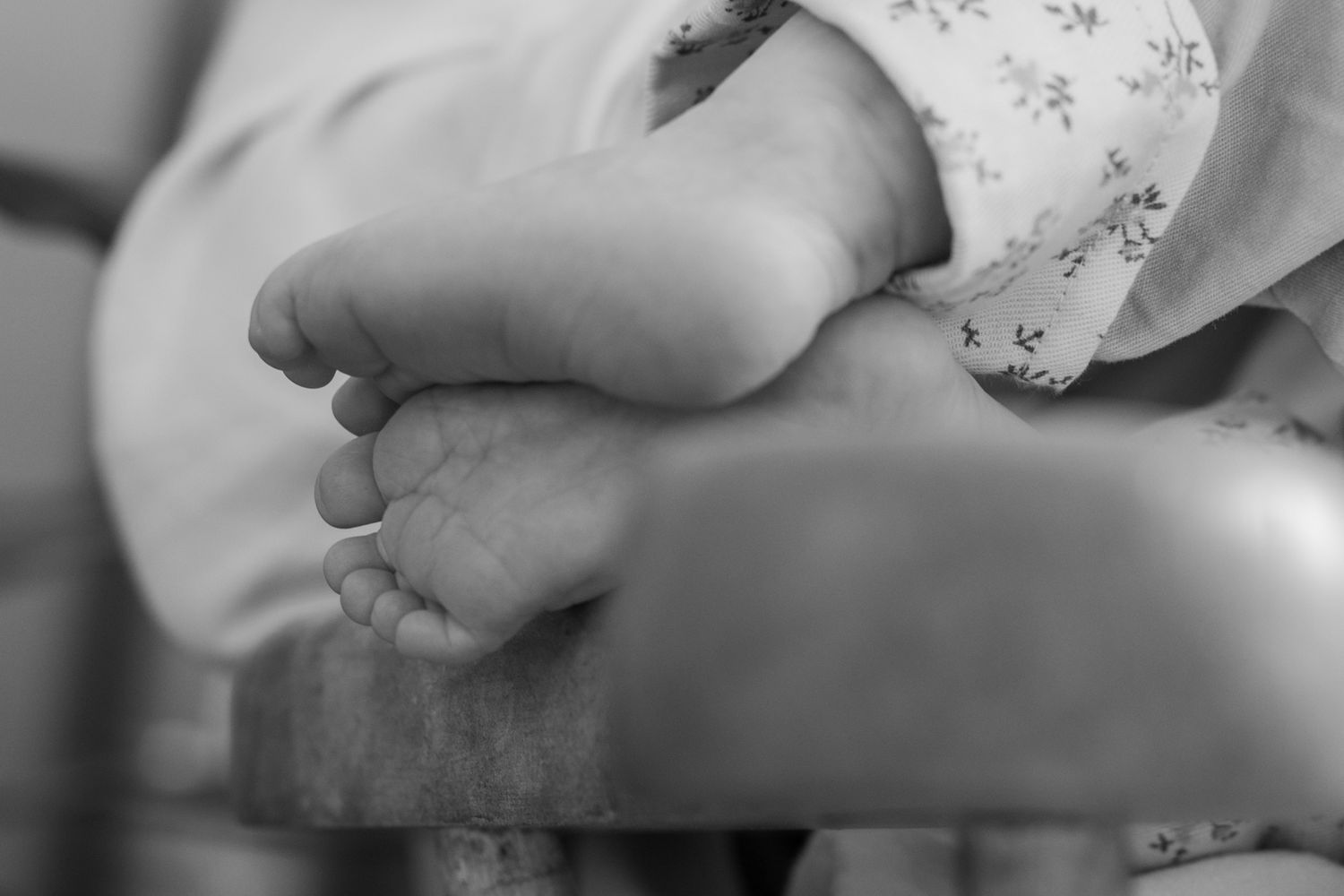 Close-up black and white photo of a newborn baby's tiny feet resting on a wooden surface.