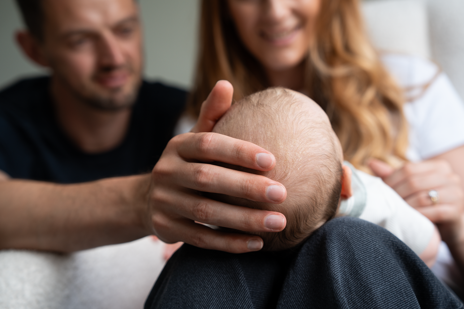 Happy parents smiling and gently cradling their newborn baby's head at home.