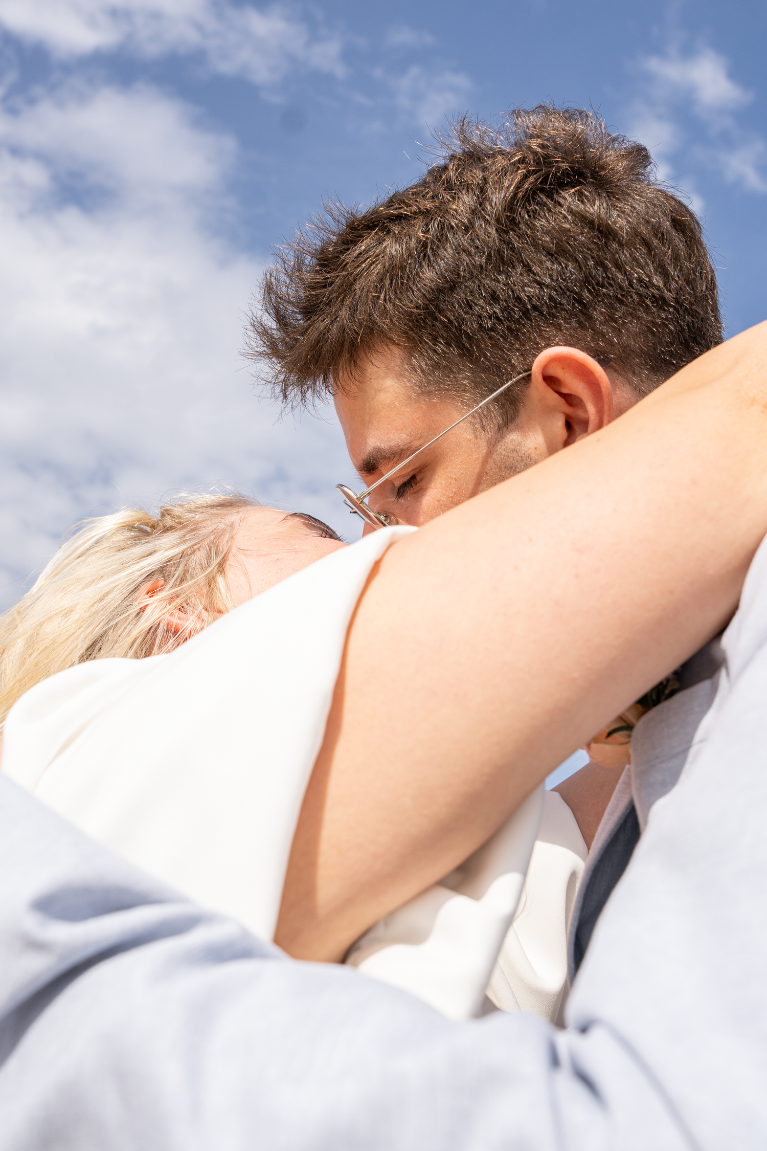 Close-up of bride and groom sharing tender embrace against blue sky on their wedding day.