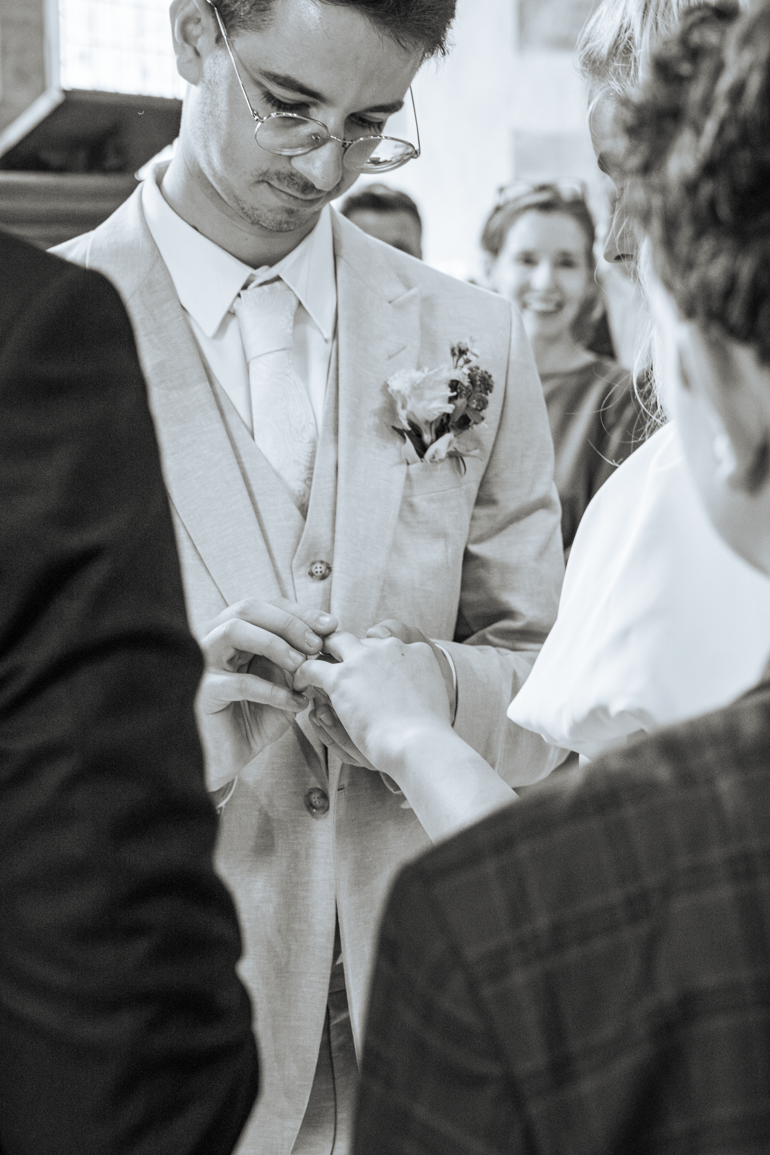 Groom in light suit with boutonniere having wedding ring placed on finger during ceremony.