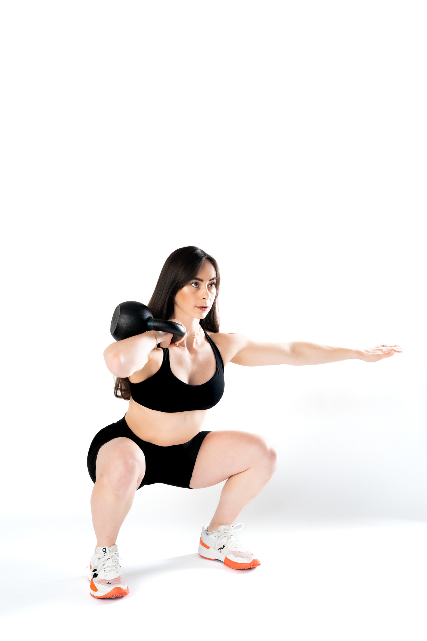Fit woman in black workout set doing a squat with a kettlebell in a white studio.
