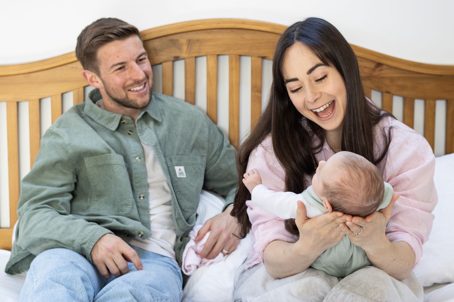 Joyful parents on bed, mother cuddling newborn baby while father watches and smiles.