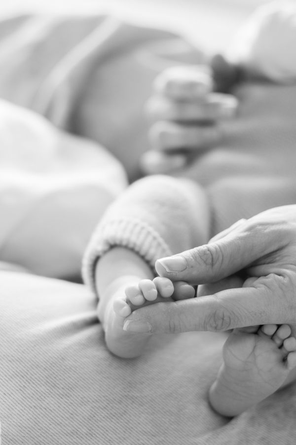 Black and white close-up of a parent's hand gently touching a newborn baby's tiny foot.