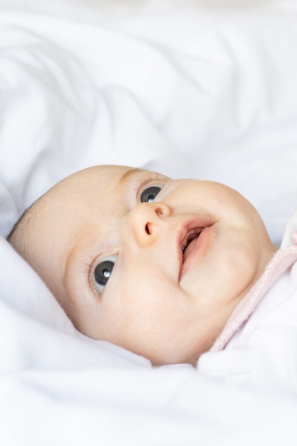 Close-up portrait of an alert newborn baby with wide eyes lying on white bedding.