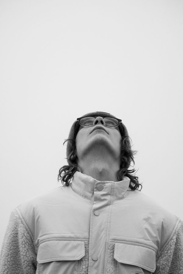 Black and white portrait of person in white jacket looking upward with glasses pushed up.