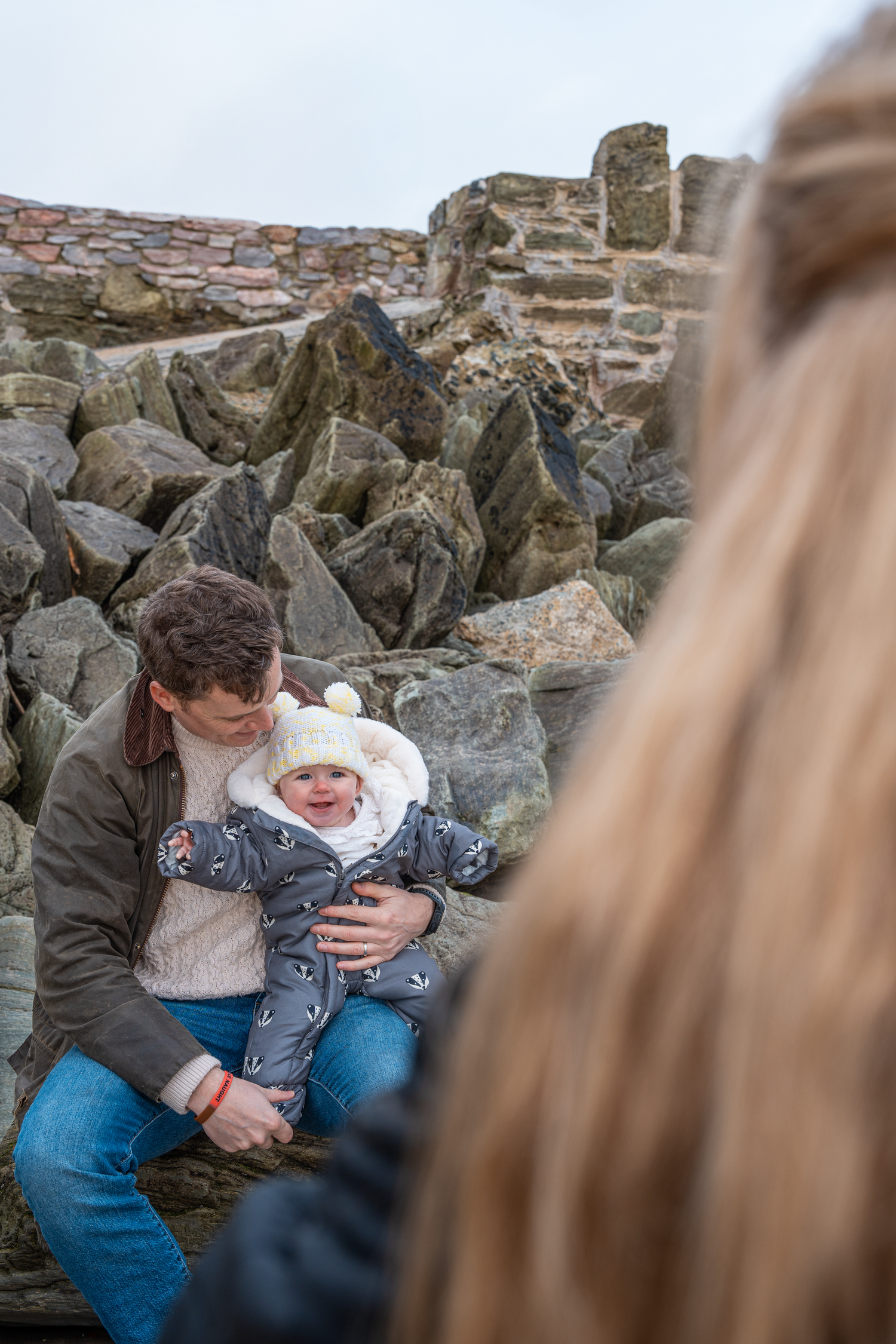 Father sitting on rocks with laughing baby in winter hat.