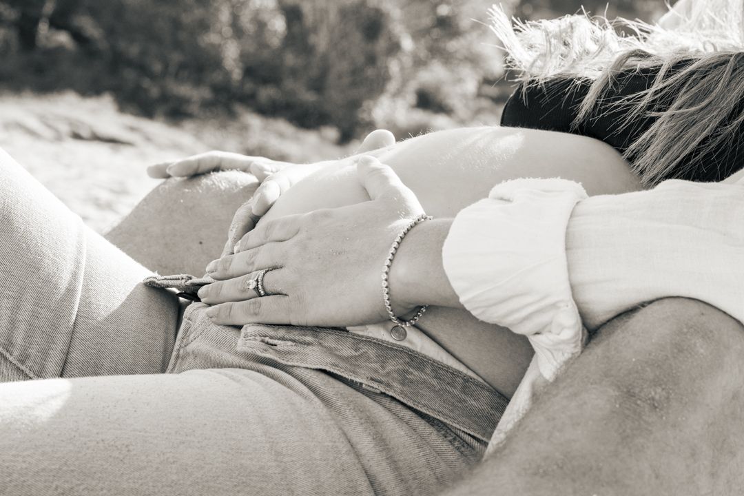 Black and white close-up of hands gently holding pregnant belly outdoors.