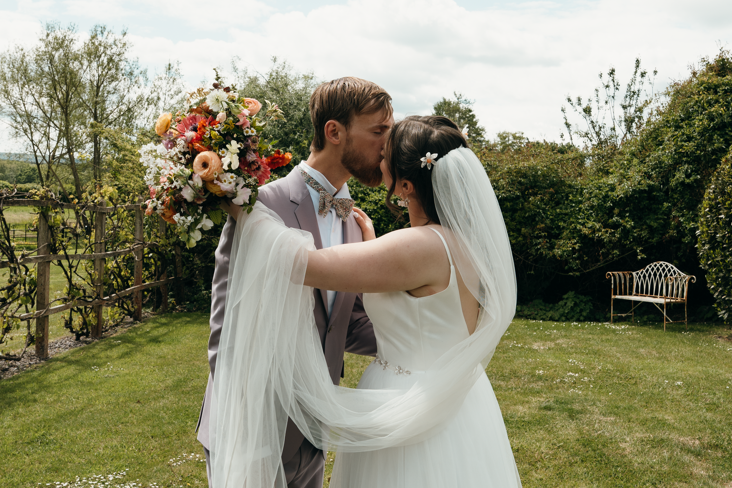 Bride and groom sharing a kiss outdoors at a garden wedding with a colorful floral arch backdrop.