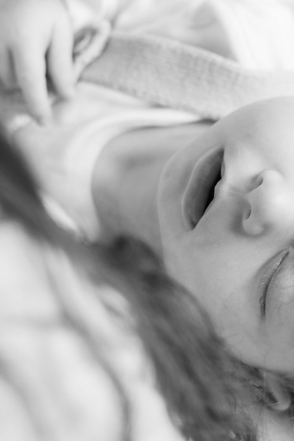 Black and white artistic close-up of a baby's serene face on white bedding.