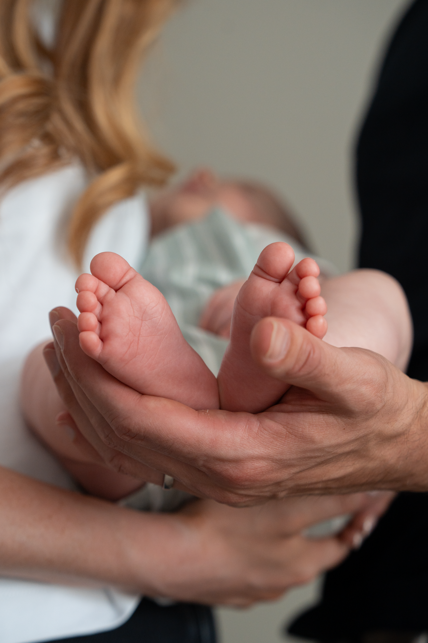 Close-up of tiny newborn baby feet cradled gently in adult hands, with mother holding infant in background.