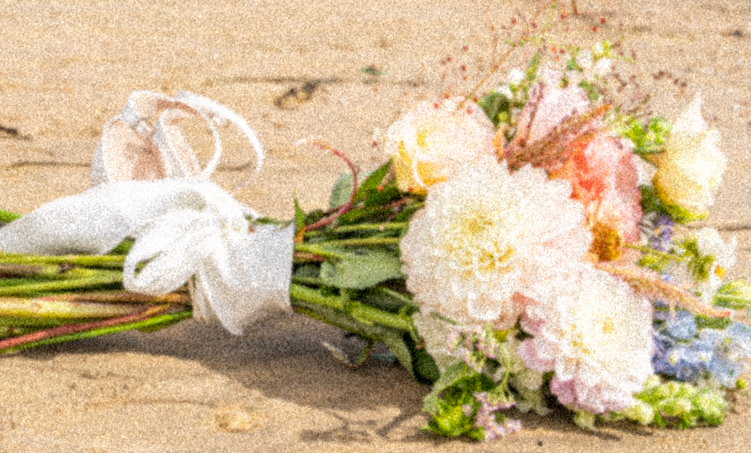 Bridal bouquet of white dahlias and pastel flowers resting on sand with a lace veil nearby.