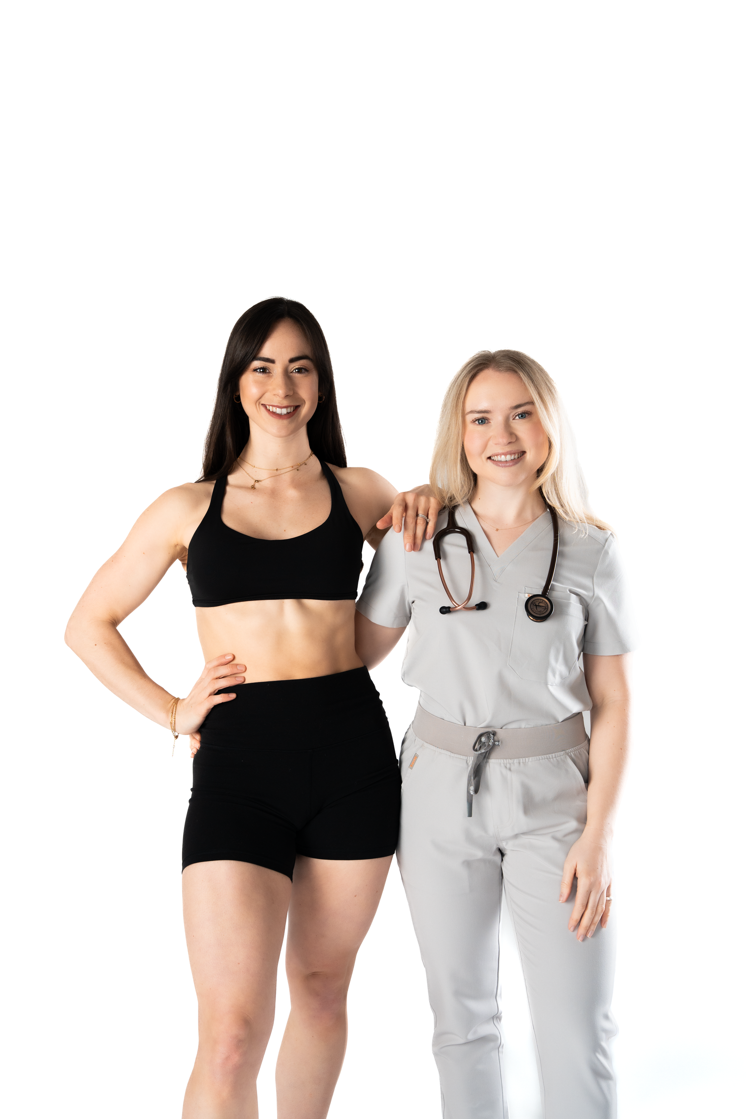 A fit woman in black athletic wear stands with a smiling female doctor in gray scrubs with a stethoscope.