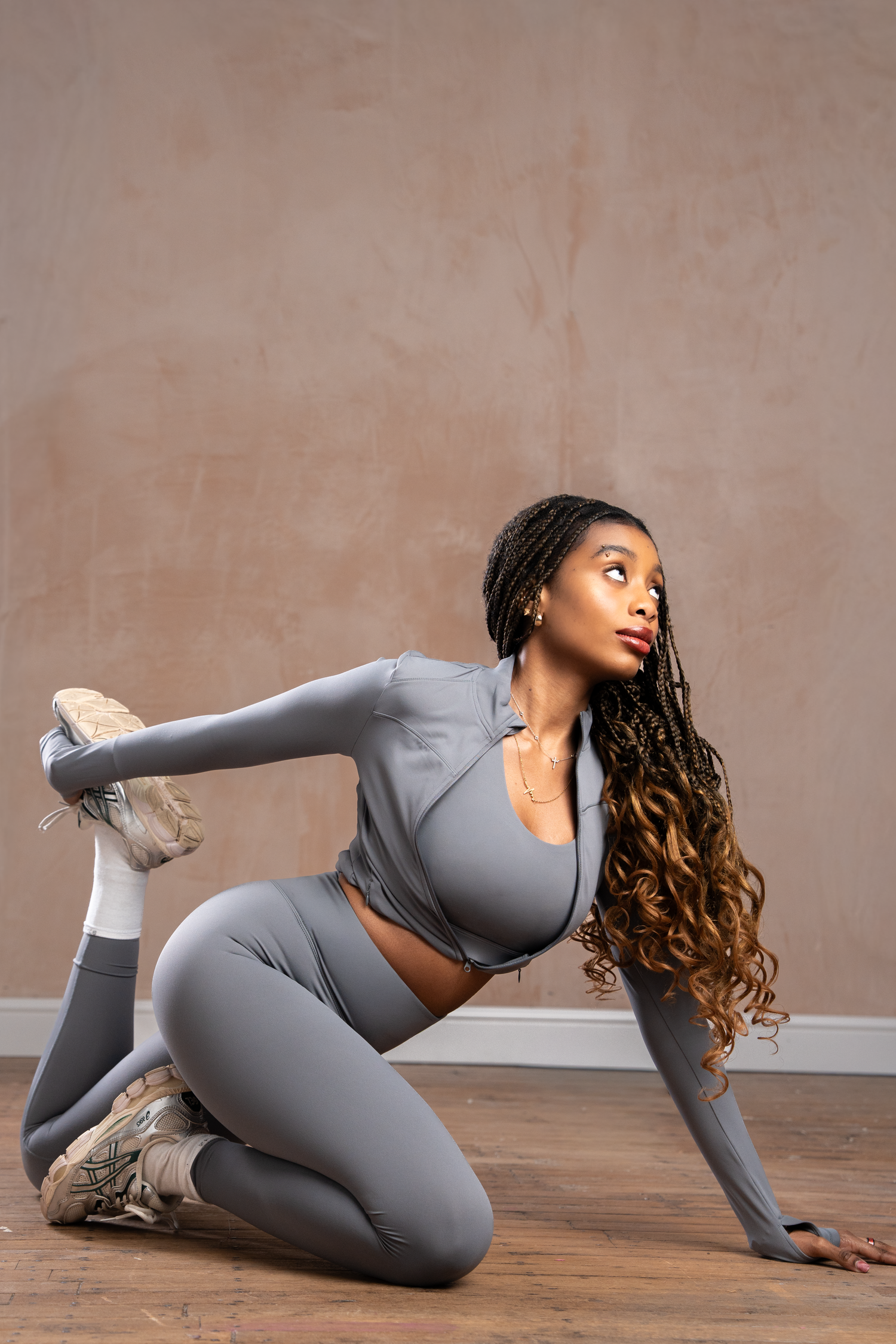 A woman in a gray athletic set poses gracefully on a studio floor, showcasing flexibility in a dynamic stretch pose.