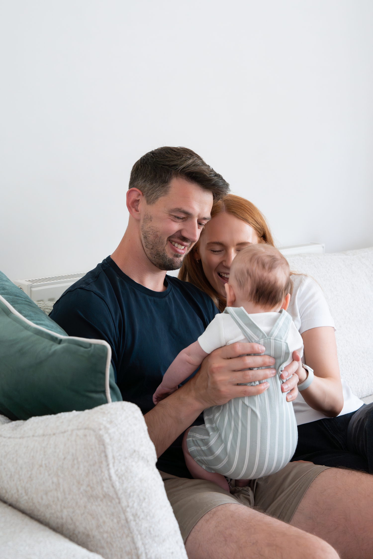 Happy young couple sitting on a sofa, smiling and bonding with their newborn baby at home.