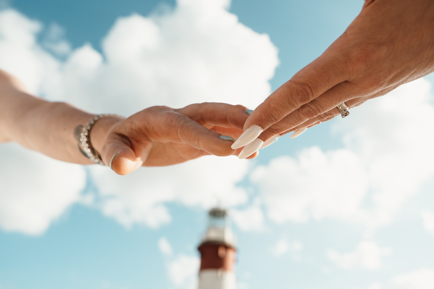 Two hands gently touching fingertips with a lighthouse and blue sky in the background.