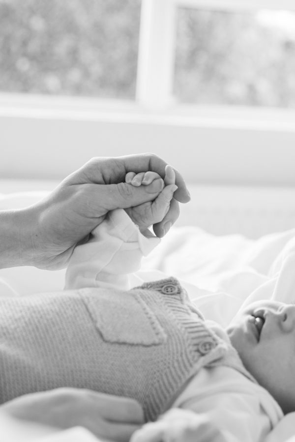 Black and white photo of an adult hand holding a newborn baby's tiny fist near a window.