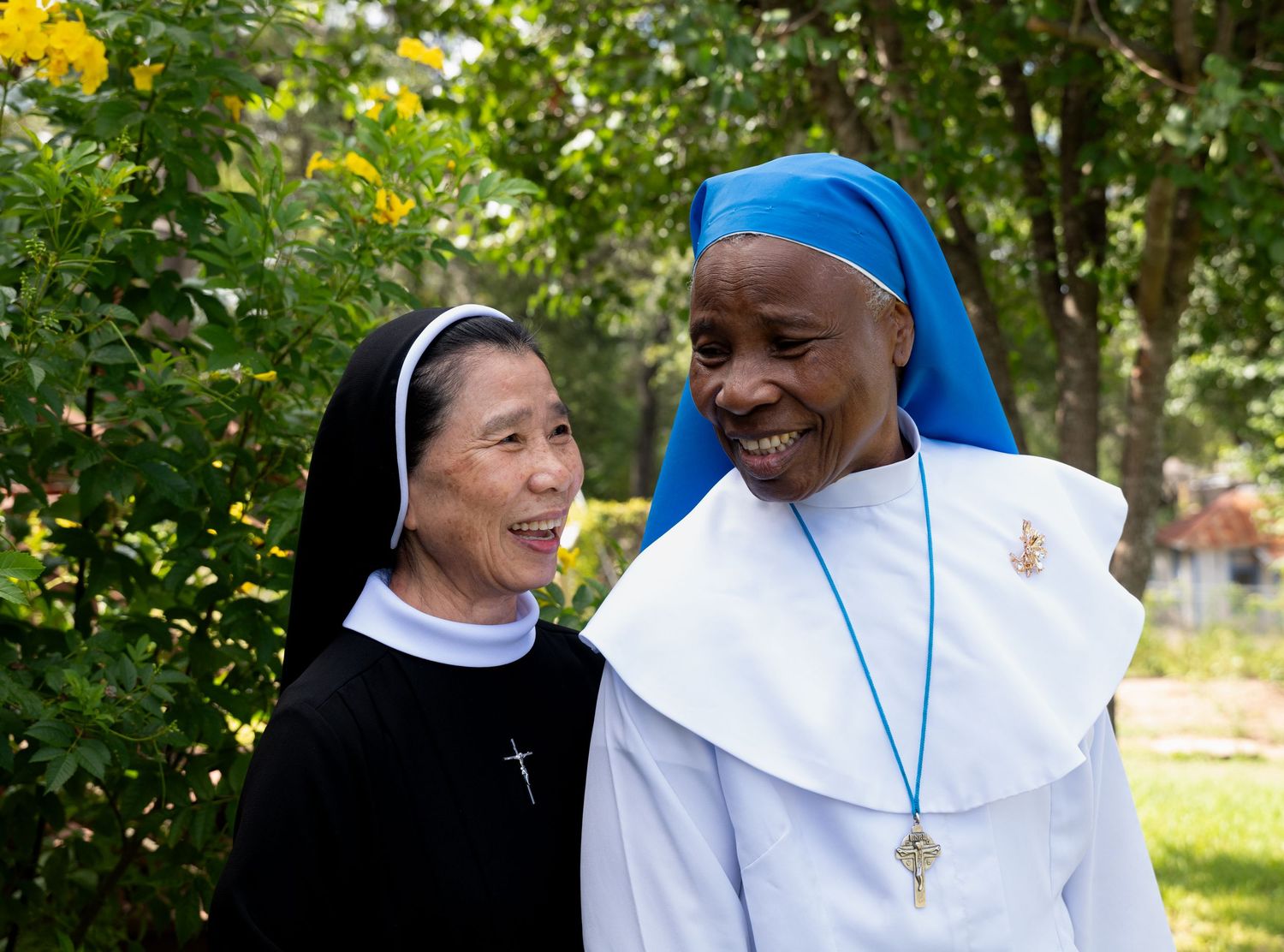 Two Catholic nuns of different backgrounds smiling and talking together outside in a peaceful garden.