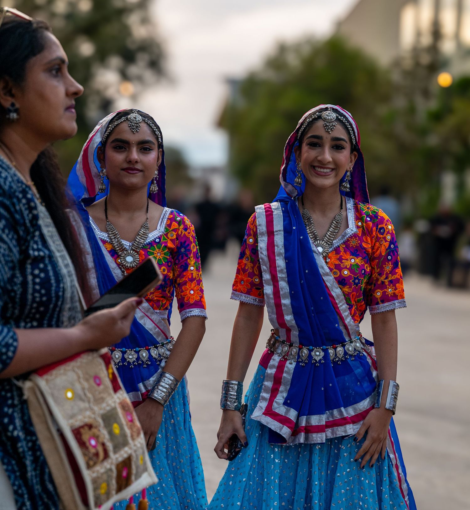 People wearing vibrant traditional dresses with blue and floral patterns gather outdoors during a cultural celebration.