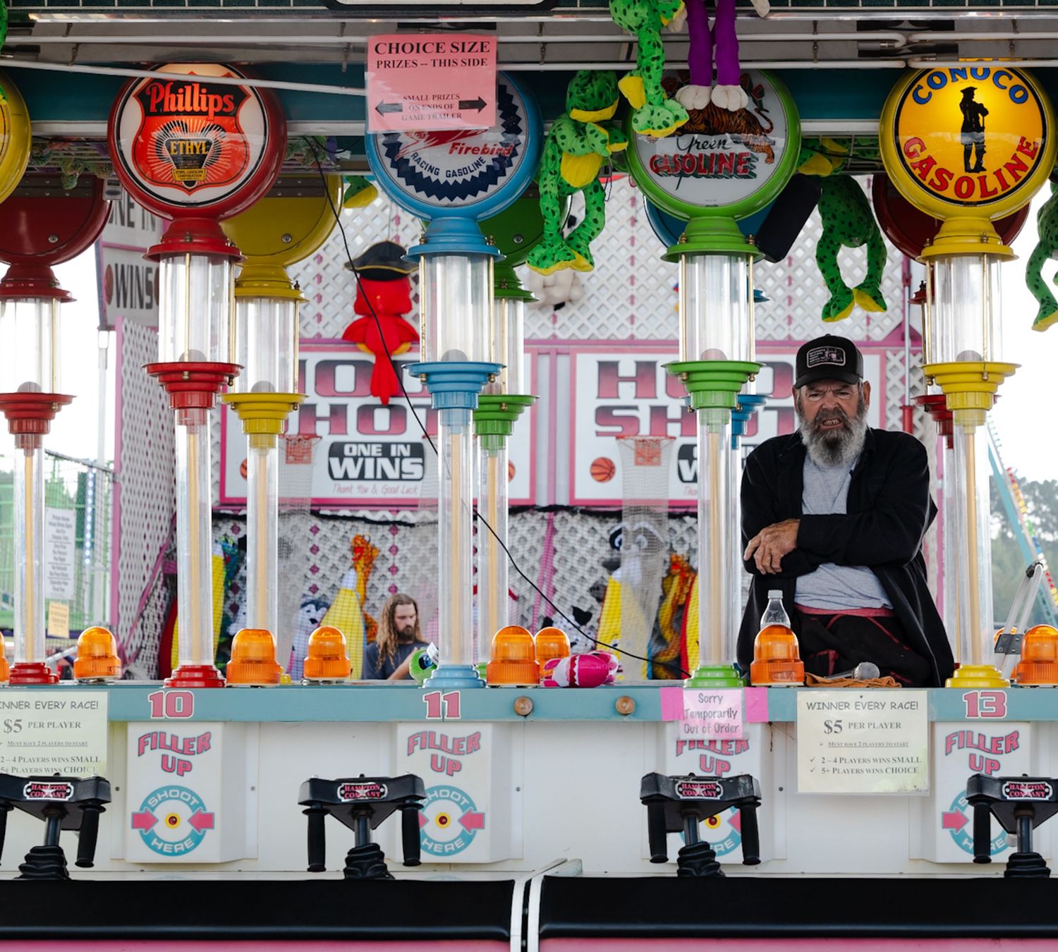 Carnival game booth with vintage gas pump–style targets and attendant waiting for players.