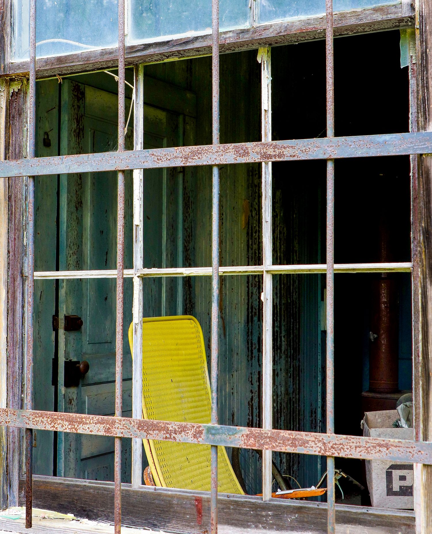 Abandoned building interior seen through a broken window with metal bars.