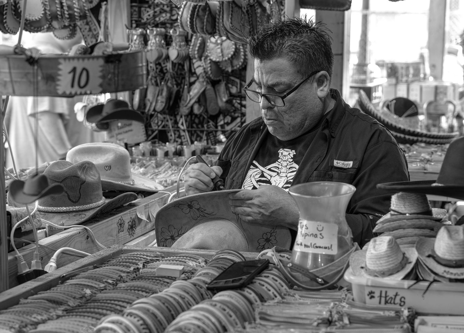 Hispanic craftsman carefully engraving a decorative hat in a busy market surrounded by handmade items and traditional goods.